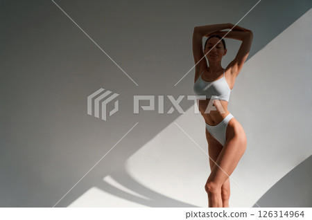 Against wall. Young caucasian woman with slim body shape is indoors in the studio Against wall. Young caucasian woman with slim body shape is indoors in the studio 126314964
