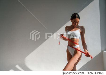Weight loss conception. With measuring tape. Young caucasian woman with slim body shape is indoors in the studio 126314968
