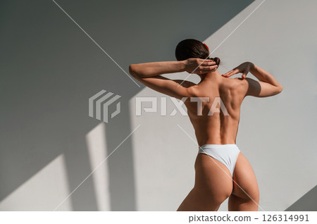 Without bra. Showing back. Young caucasian woman with slim body shape is indoors in the studio Without bra. Showing back. Young caucasian woman with slim body shape is indoors in the studio 126314991