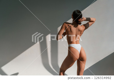 Without bra. Showing back. Young caucasian woman with slim body shape is indoors in the studio Without bra. Showing back. Young caucasian woman with slim body shape is indoors in the studio 126314992
