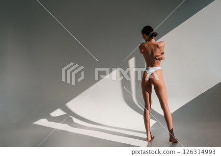 Posing, showing the back, without bra. Young caucasian woman with slim body shape is indoors in the studio Posing, showing the back, without bra. Young caucasian woman with slim body shape is indoors in the studio 126314993