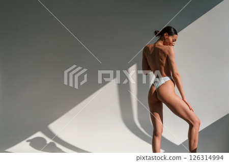 Posing, showing the back, without bra. Young caucasian woman with slim body shape is indoors in the studio Posing, showing the back, without bra. Young caucasian woman with slim body shape is indoors in the studio 126314994
