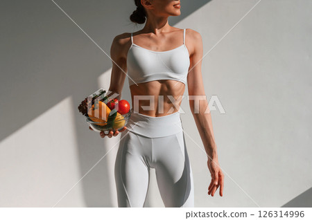 Holding vegetables and fruits. Young caucasian woman with slim body shape is indoors in the studio Holding vegetables and fruits. Young caucasian woman with slim body shape is indoors in the studio 126314996