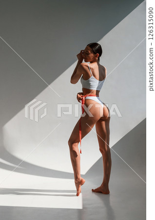 Showing the back. Young caucasian woman with slim body shape is indoors in the studio 126315090