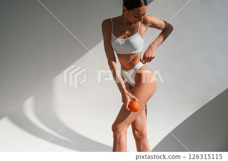 Young caucasian woman with slim body shape is indoors in the studio. Holding an orange 126315115