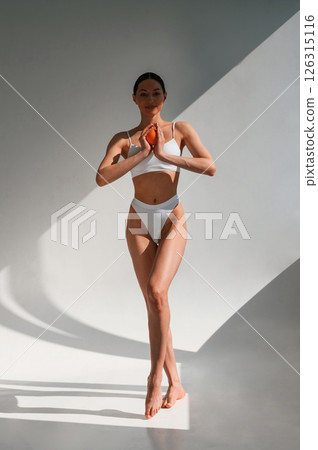 Young caucasian woman with slim body shape is indoors in the studio. Holding an orange Young caucasian woman with slim body shape is indoors in the studio. Holding an orange 126315116