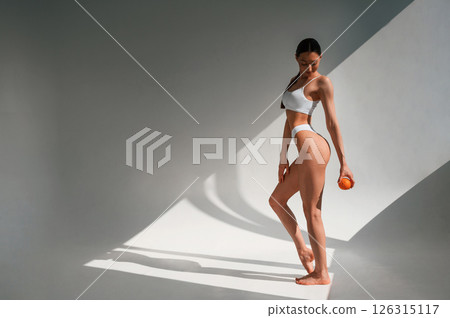 Young caucasian woman with slim body shape is indoors in the studio. Holding an orange Young caucasian woman with slim body shape is indoors in the studio. Holding an orange 126315117