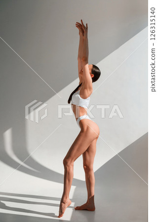 Standing with hands up. Young caucasian woman with slim body shape is indoors in the studio 126315140