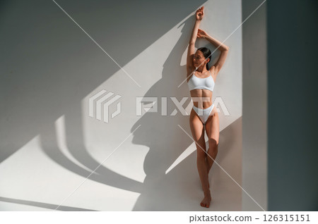 Leaning on the wall. Young caucasian woman with slim body shape is indoors in the studio Leaning on the wall. Young caucasian woman with slim body shape is indoors in the studio 126315151
