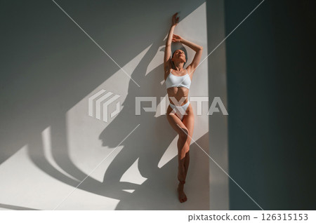 Leaning on the wall. Young caucasian woman with slim body shape is indoors in the studio Leaning on the wall. Young caucasian woman with slim body shape is indoors in the studio 126315153