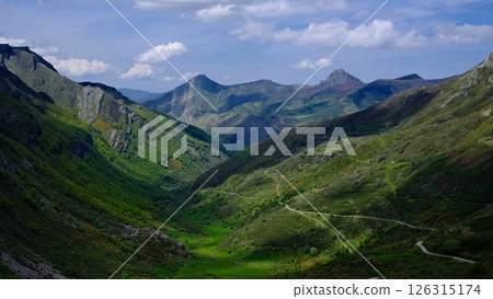 Scenic panoramic view of a lush green valley surrounded by dramatic mountain peaks under a partly cloudy sky Scenic panoramic view of a lush green valley surrounded by dramatic mountain peaks under a partly cloudy sky 126315174