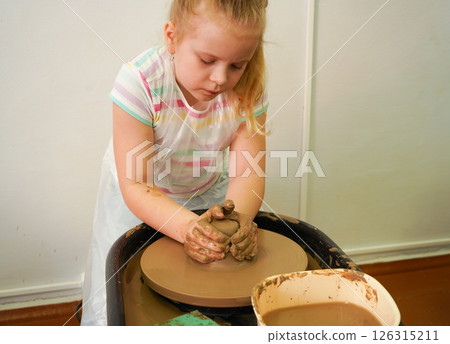Child hands make earthenware cup working on pottery wheel at workshop. 126315211