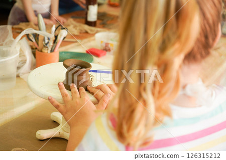 Kids arts and crafts class in workshop. Little girl creating cup and bowl of clay. Creative activity for young children in school. Cute kid forming toy with ceramic. 126315212