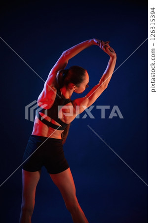 Stretching the hands. Beautiful muscular woman is indoors in the studio with neon lighting 126315394