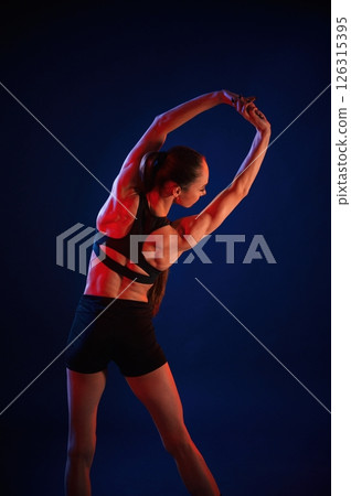 In studio with red and blue neon lighting. Beautiful muscular woman is indoors In studio with red and blue neon lighting. Beautiful muscular woman is indoors 126315395