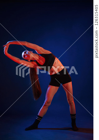 Warm up exercises. Beautiful muscular woman is indoors in the studio with neon lighting 126315405