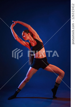 Fitness exercises. Beautiful muscular woman is indoors in the studio with neon lighting Fitness exercises. Beautiful muscular woman is indoors in the studio with neon lighting 126315412