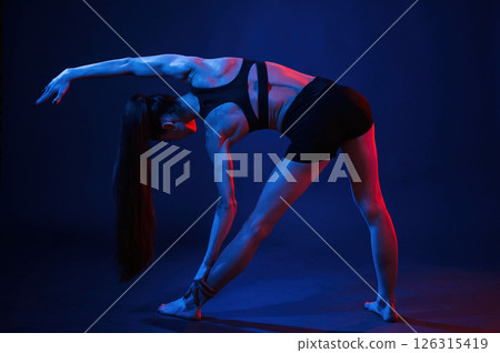 Doing sportive exerises. Beautiful muscular woman is indoors in the studio with neon lighting 126315419