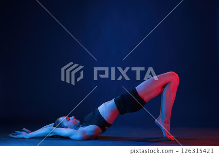 View from the side, lying down on the floor. Beautiful muscular woman is indoors in the studio with neon lighting 126315421