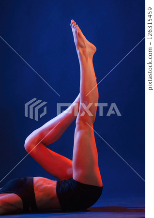 View from the side, lying down on the floor. Beautiful muscular woman is indoors in the studio with neon lighting View from the side, lying down on the floor. Beautiful muscular woman is indoors in the studio with neon lighting 126315459