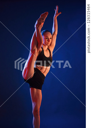 Leg stretching. Beautiful muscular woman is indoors in the studio with neon lighting 126315464