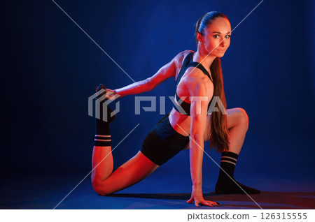 Fitness exercises. Beautiful muscular woman is indoors in the studio with neon lighting 126315555