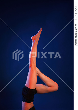 Shoulder stand. Beautiful muscular woman is indoors in the studio with neon lighting Shoulder stand. Beautiful muscular woman is indoors in the studio with neon lighting 126315560