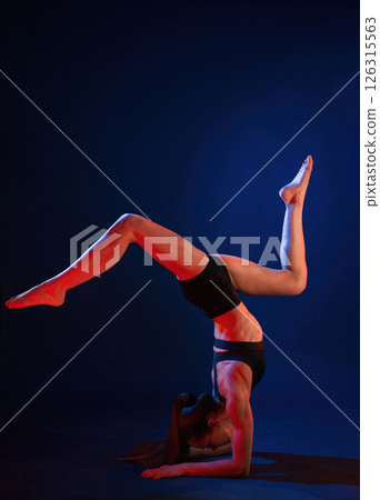 Doing hand stand. Beautiful muscular woman is indoors in the studio with neon lighting Doing hand stand. Beautiful muscular woman is indoors in the studio with neon lighting 126315563