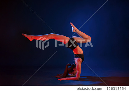Doing hand stand. Beautiful muscular woman is indoors in the studio with neon lighting Doing hand stand. Beautiful muscular woman is indoors in the studio with neon lighting 126315564