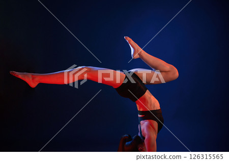 Doing hand stand. Beautiful muscular woman is indoors in the studio with neon lighting Doing hand stand. Beautiful muscular woman is indoors in the studio with neon lighting 126315565