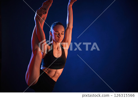Raising up the leg, exercise. Beautiful muscular woman is indoors in the studio with neon lighting Raising up the leg, exercise. Beautiful muscular woman is indoors in the studio with neon lighting 126315566