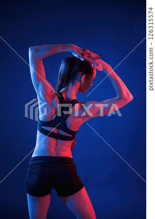 Rear view. Beautiful muscular woman is indoors in the studio with neon lighting 126315574