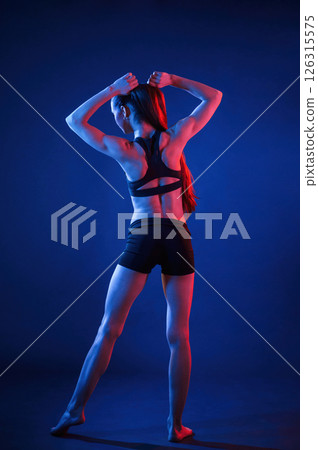 Rear view. Beautiful muscular woman is indoors in the studio with neon lighting 126315575
