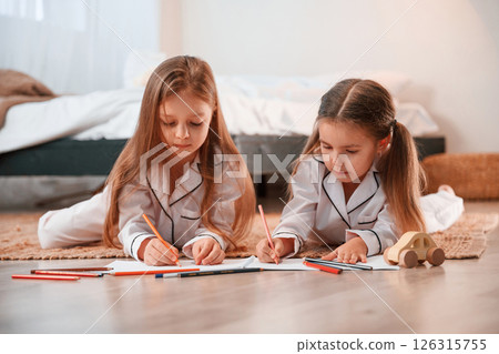 Two little girls are lying down on the ground and drawing together in domestic room 126315755