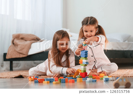 Construction toys is on the ground. Two little girls are playing and having fun together in domestic room 126315756