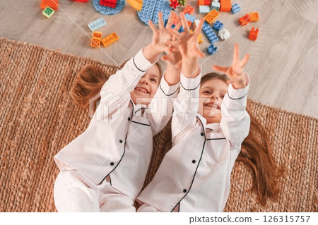 With hands up. Lying down on the floor. Two little girls are playing and having fun together in domestic room With hands up. Lying down on the floor. Two little girls are playing and having fun together in domestic room 126315757