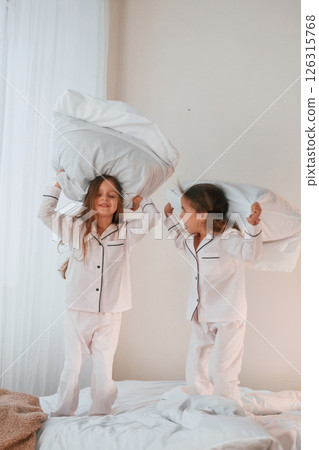Playing pillow fight. Two little girls are having fun together in domestic room Playing pillow fight. Two little girls are having fun together in domestic room 126315768