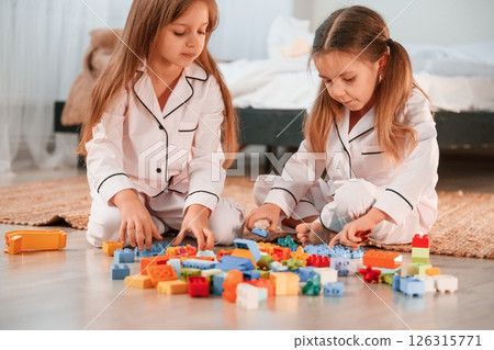 Construction toys is on the ground. Two little girls are playing and having fun together in domestic room Construction toys is on the ground. Two little girls are playing and having fun together in domestic room 126315771