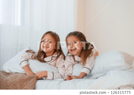 Lying down on the bed. Two little girls are playing and having fun together in domestic room Lying down on the bed. Two little girls are playing and having fun together in domestic room 126315775