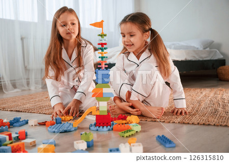 Toy building by construction toys. Two little girls are playing and having fun together in domestic room 126315810