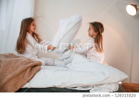 On the bed. Pillow fight. Two little girls are playing and having fun together in domestic room 126315820