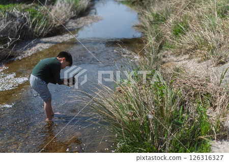 一個男孩在春日的陽光下在河裡玩耍 126316327