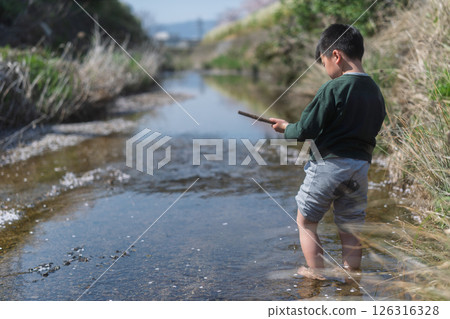 一個男孩在春日的陽光下在河裡玩耍 126316328