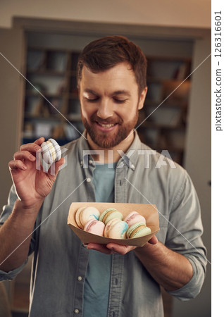 Smiling, positive emotions. Man in casual clothes is holding macarons that are in the paper eco box 126316601