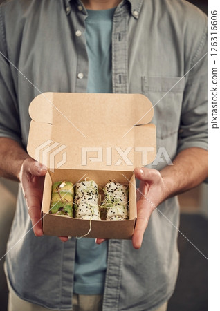 Man in casual clothes is holding sushi that is in the paper eco box Man in casual clothes is holding sushi that is in the paper eco box 126316606