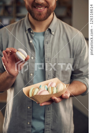 Holding and showing macaron. Man in casual clothes is holding sweets that are in the paper eco box 126316614