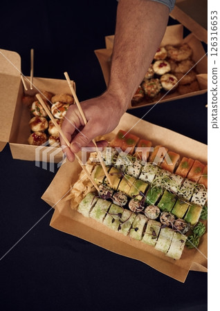 Using chopsticks. Man in casual clothes is with sushi that is in the paper eco box 126316653