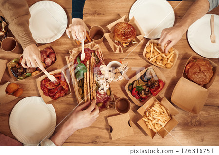 Top view of table with food on it, hands of the people taking it, eating. Meat, vegetables, French fries, burger, mushrooms Top view of table with food on it, hands of the people taking it, eating. Meat, vegetables, French fries, burger, mushrooms 126316751