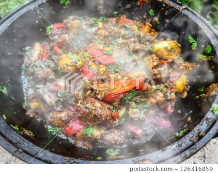 Delicious spicy beef stew cooking in a traditional pot outdoors with fresh vegetables and herbs Delicious spicy beef stew cooking in a traditional pot outdoors with fresh vegetables and herbs 126316859