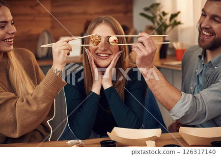 Having fun, rolls of the food in the front of the eyes of woman. Friends are sitting indoors at home and eating sushi together 126317140
